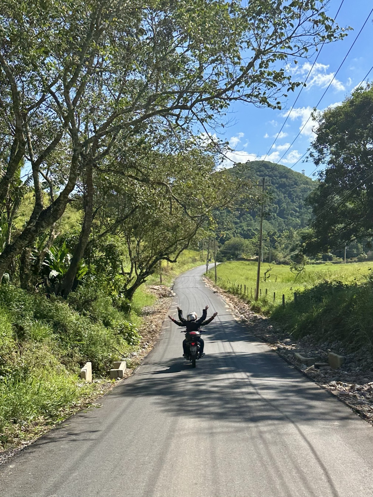 Passenger and guide with their arms up on a quiet country road, hills ahead