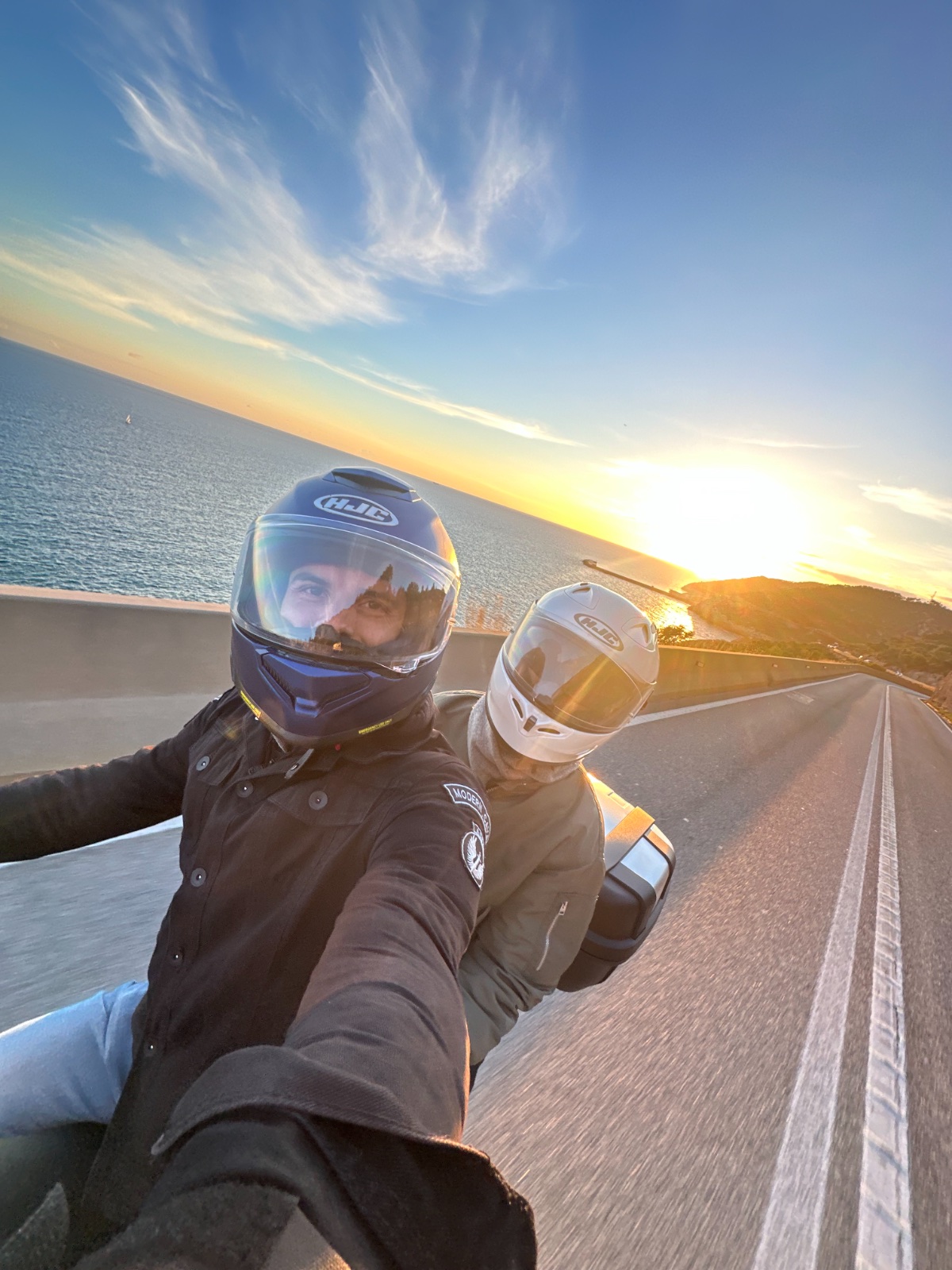 Rider and passenger on the Garraf coast road at sunset, the Mediterranean behind them