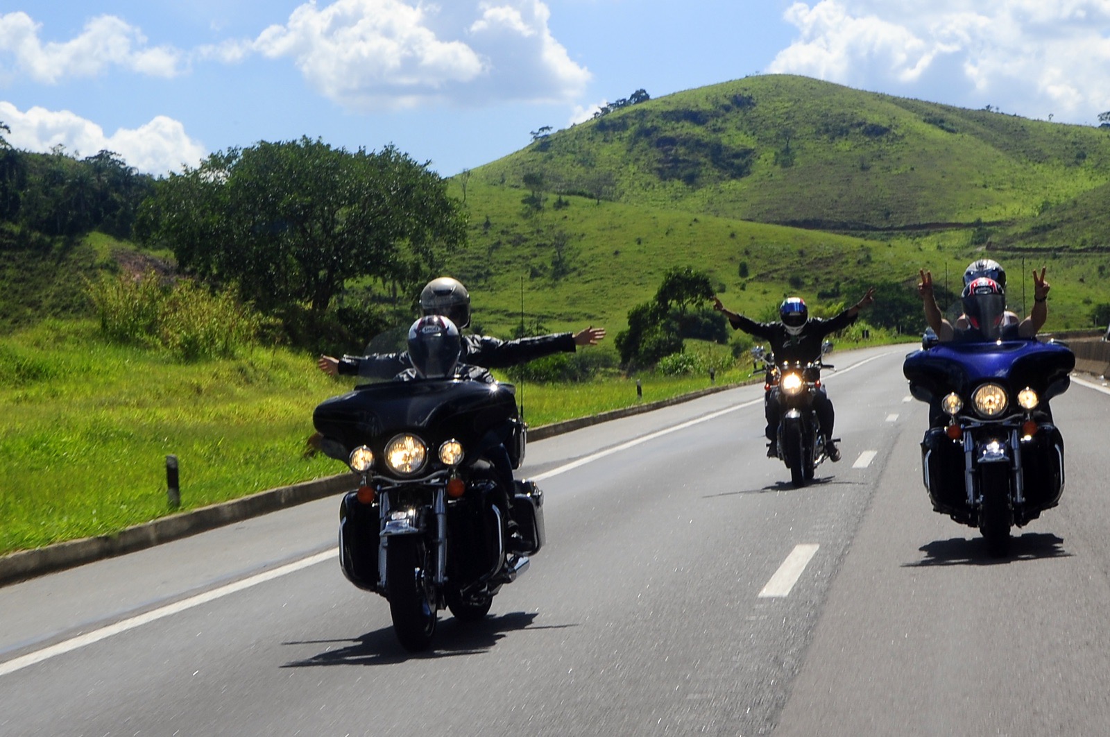 Passenger with arms wide open on the back of a touring motorcycle, green hills around