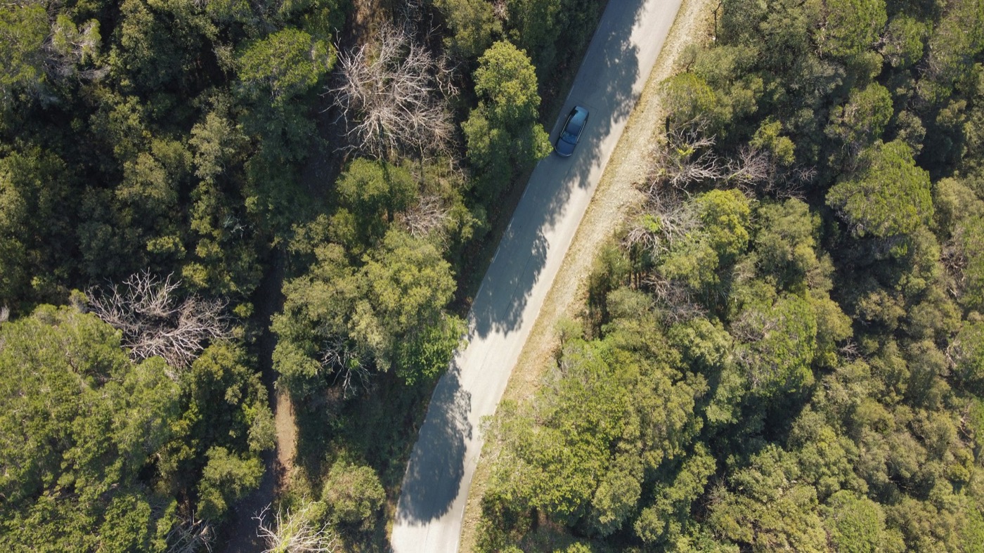 A mountain road seen from above, running through thick forest