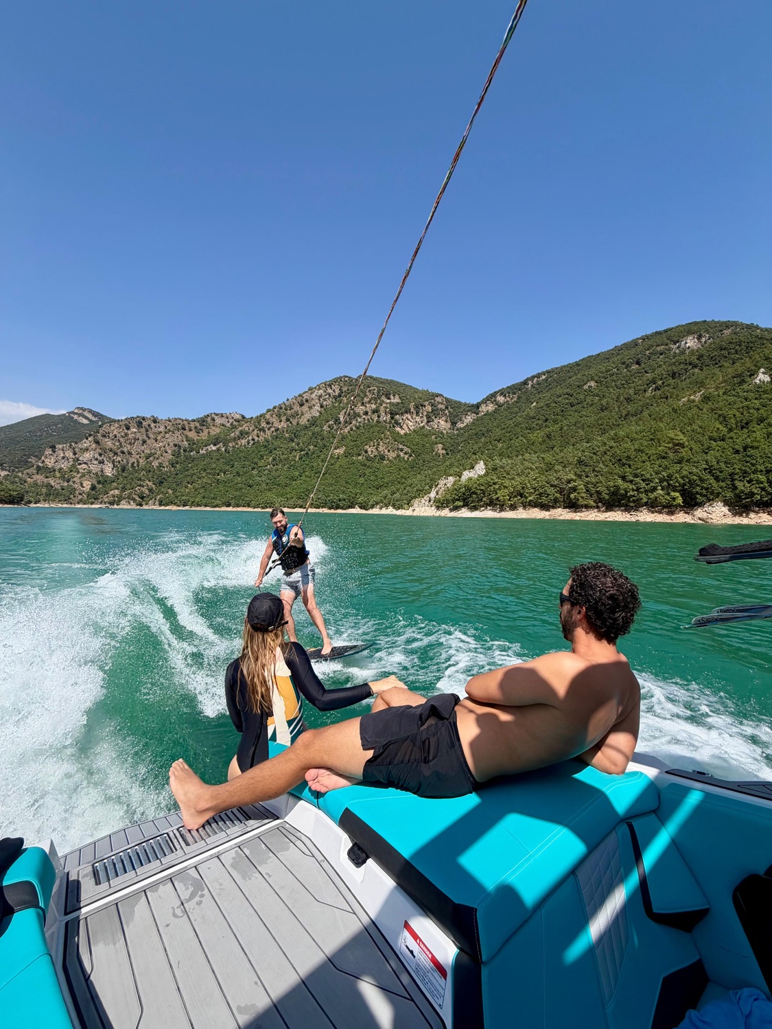 View from the back of the wake boat: a rider on the wave, mountains around the lake