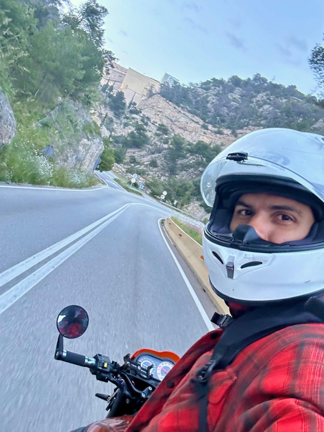 A rider in a white helmet on the Garraf road, the curve and the green hillside behind