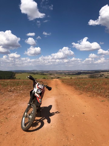 Red dirt road running through open farmland under tall clouds, Brazil