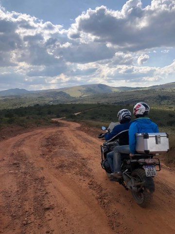 Two riders on a red dirt road with the hills of southern Minas Gerais behind
