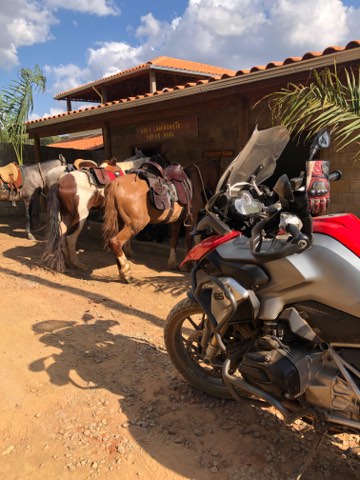 Saddled horses beside a motorcycle outside a farm building in Minas Gerais