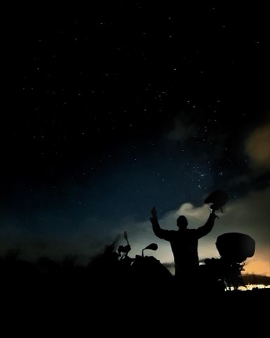 Rider silhouetted beside a motorcycle under a star-filled sky in Carrancas