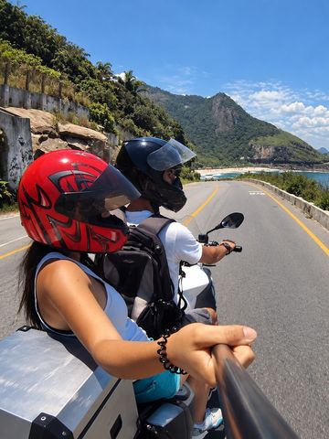 Pasajera y piloto en una moto por la carretera de la costa de Río de Janeiro, con el océano a la derecha