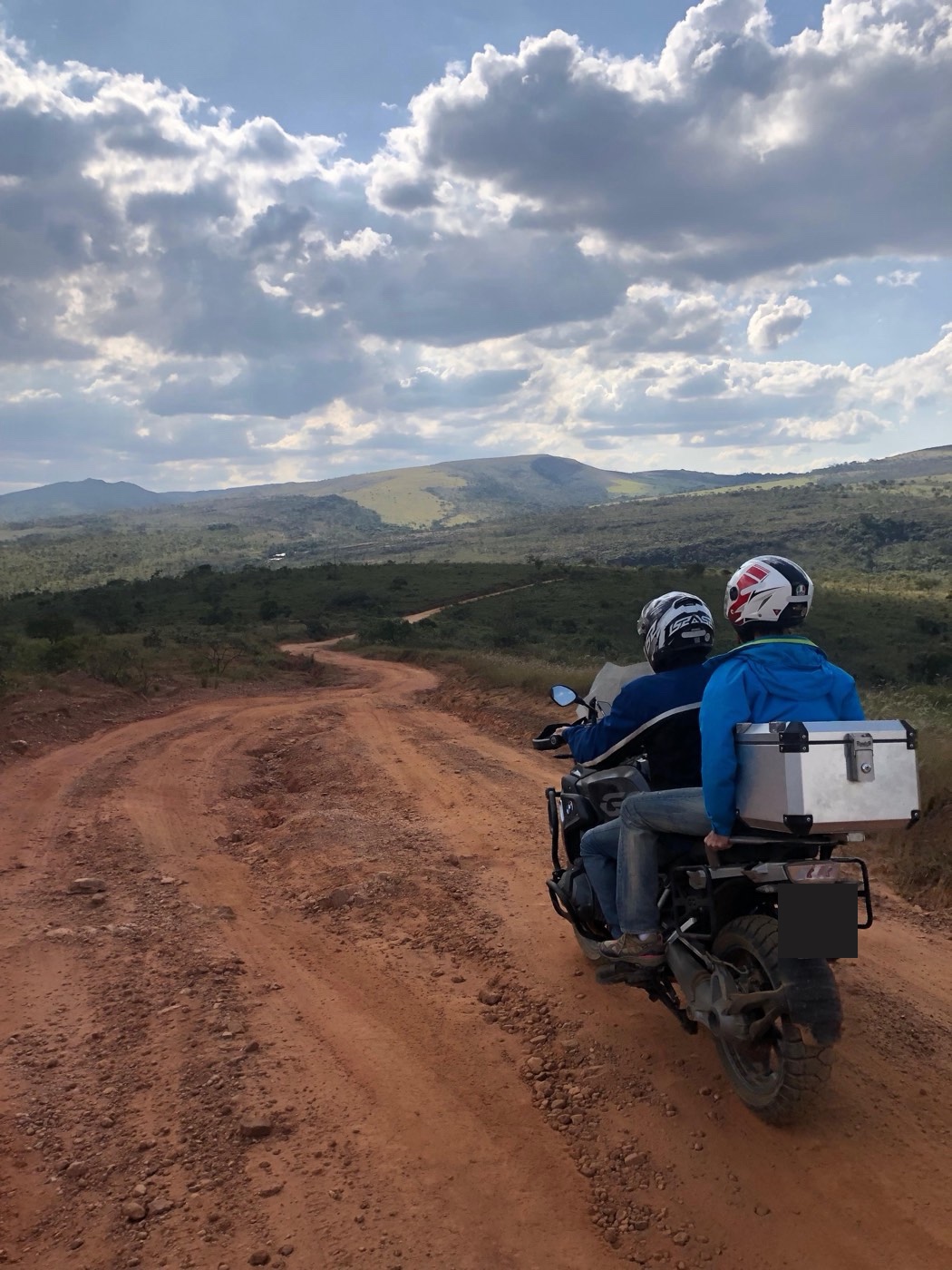 Rider and passenger on a dirt road, hills on the horizon