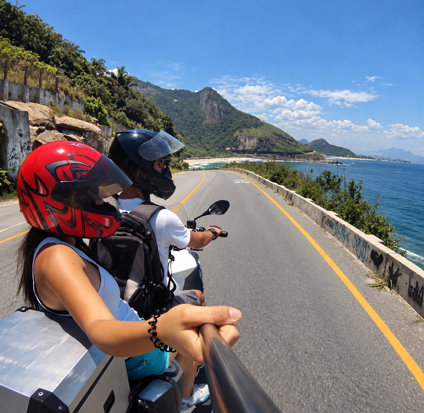 Passenger in a red helmet on the ocean road in Rio, beach and mountains ahead