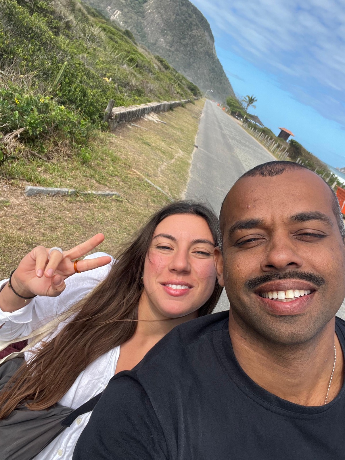 Passenger and pilot smiling in a selfie on a coastal road in Rio